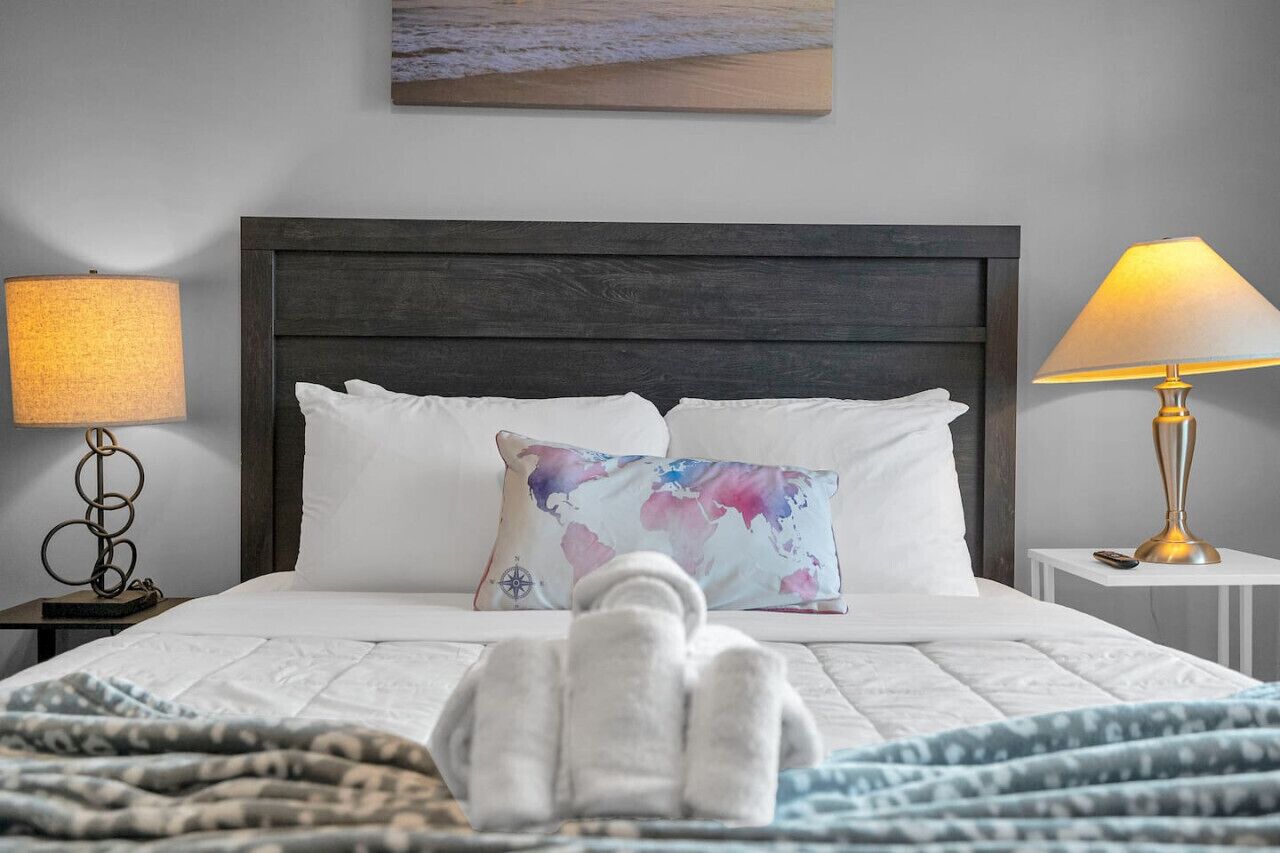 Un lit bien fait, avec des draps blancs, un coussin décoratif et une serviette pliée posée sur le lit.
