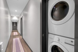 Une buanderie équipée d’un lave-linge et d’un sèche-linge, avec un plancher en bois et un couloir menant à une porte.