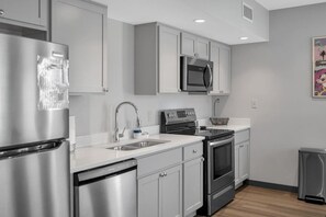 Une cuisine moderne dotée d’appareils électroménagers en acier inoxydable, de meubles de rangement gris et d’un plan de travail blanc.