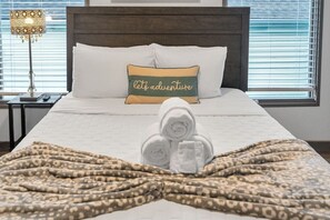 Un lit bien fait, avec un oreiller orné de l’inscription « partons à l’aventure », une serviette roulée et une couverture à motifs léopard.