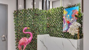 A reception area with a wall covered in green foliage, a pink flamingo sculpture, a marble reception desk, and a colorful painting.