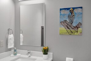 Een badkamer met een grote spiegel, een wastafel, een handdoekhouder en een schilderij van een pelikaan op een tak.