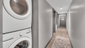A laundry room with stacked washers and dryers, a patterned rug, and a hallway leading to a door.