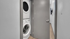 Ein moderner Waschraum mit einer Frontlader-Waschmaschine und einem Trockner, einer grauen Tür und einem sichtbaren Lichtschalter.