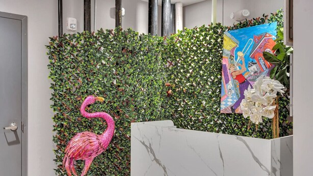 Ein Empfangsbereich mit einer Wand, die mit Grünpflanzen bewachsen ist, einer rosa Flamingo-Skulptur, einem Marmor-Rezeptionstresen und einem farbenfrohen Gemälde.