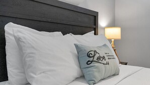 Ein ordentlich bezogenes Bett mit weißen Leinen und einem dekorativen Kissen mit dem Wort 'Love' und einem Zitat.