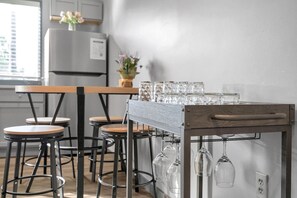 Una cocina con una mesa de madera y taburetes de bar, una estantería para vinos con copas y un refrigerador.