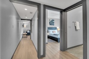 Un pasillo moderno de hotel con piso de madera, una cama con cabecera azul y una obra de arte colgada en la pared.