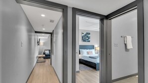 A modern hotel hallway with a wooden floor, a bed with a blue headboard, and a wall-mounted artwork. - Cozy New Build - 5min to FQ/Frenchman+Parking (New Orleans)