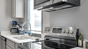 A modern kitchen with a stainless steel stove, a sink, and a window with a city view. - Cozy New Build - 5min to FQ/Frenchman+Parking (New Orleans)