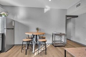 Eine moderne Küche mit einem runden Holztisch, vier Barhocker, einem Edelstahlkühlschrank und einem Metallwagen mit Gläsern.