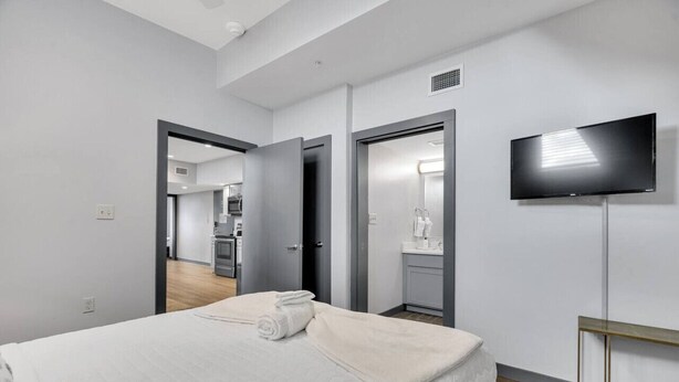 Ein modernes Hotelzimmer mit einem großen Bett, einem Fernseher und einer Küchenzeile im Hintergrund.