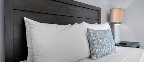 Una cama con almohadas blancas y estampadas, un cabecero de madera oscura y una mesita de noche con una lámpara.