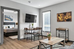 Ein modernes Hotelzimmer mit Bett, Fernseher, Essbereich mit Stühlen, Couchtisch und Wandbildern.