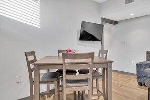 Ruokailutilassa on puinen pöytä ja tuolit, seinälle asennettu taulutelevisio sekä pieni sininen nojatuoli.
