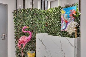 Un espace d’accueil agrémenté d’un mur recouvert de verdure, d’une sculpture représentant un flamant rose, d’un comptoir d’accueil en marbre et d’un tableau aux couleurs vives.