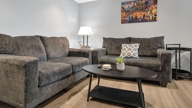 A modern living room with two grey sofas, a round coffee table, a lamp, and a colorful painting on the wall. - Bywater Haven: Near FQ&Frenchman + Secure Parking (New Orleans)