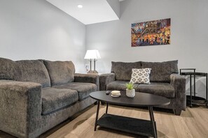 A modern living room with two grey sofas, a round coffee table, a lamp, and a colorful painting on the wall. - Bywater Haven: Near FQ&Frenchman + Secure Parking (New Orleans)