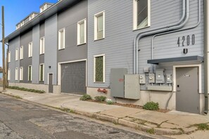 Un edificio residencial de varios pisos con fachada gris, numerado 4200, que cuenta con un acceso con portón, un cuadro de servicios y un pequeño jardín con flores rojas.