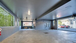 A spacious indoor area with a concrete floor, large windows on one side, and a view of a red vehicle outside. - Bywater Haven: Near FQ&Frenchman + Secure Parking (New Orleans)