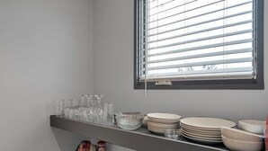 A kitchen with a window, a shelf with glassware, plates, and bowls.