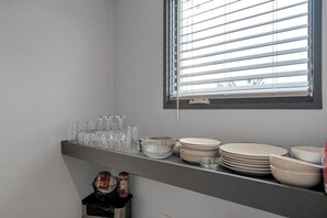 Une cuisine avec une fenêtre, une étagère où sont rangés des verres, des assiettes et des bols.