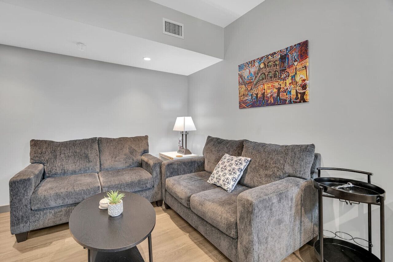 A modern living room with two grey sofas, a small round table with a plant, a floor lamp, and a colorful abstract painting on the wall.