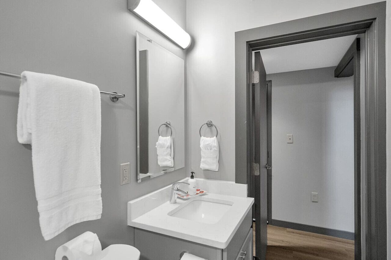 Un baño moderno con un lavamanos blanco, dos anillas para toallas, un espejo y una toalla colgada en un perchero.