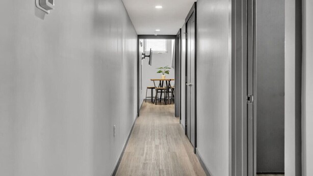 A narrow hallway with a wooden floor, a table with chairs, and a potted plant in the background.