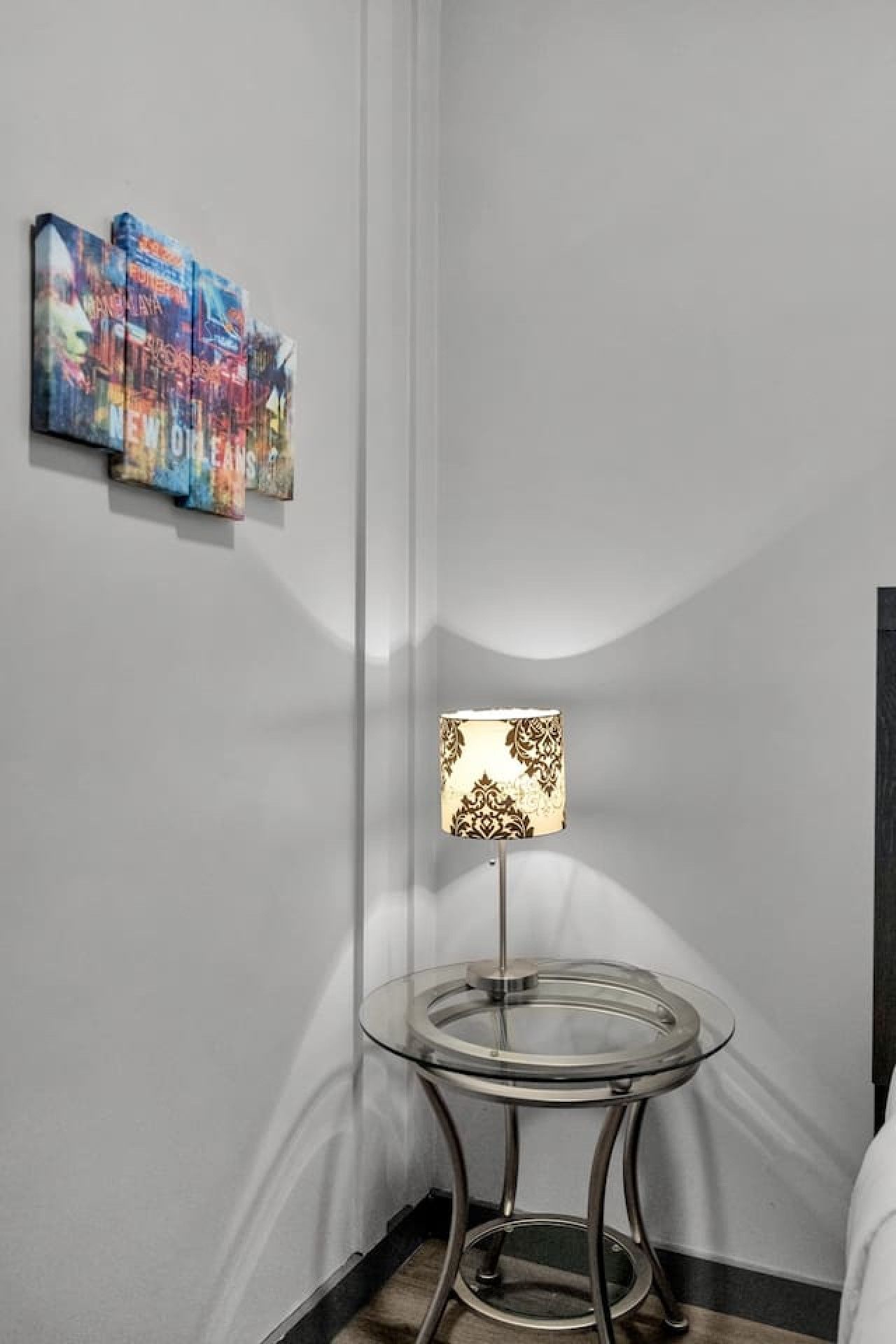 A corner of a room with a glass table lamp and a wall with colorful artwork.