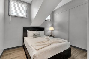 Ein modernes Schlafzimmer mit einem Bett, einer Nachttischlampe und einem Fenster mit Jalousien.