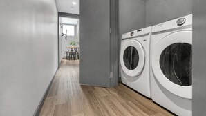 A laundry room with two white front-loading washing machines, a grey door, and a wooden floor.