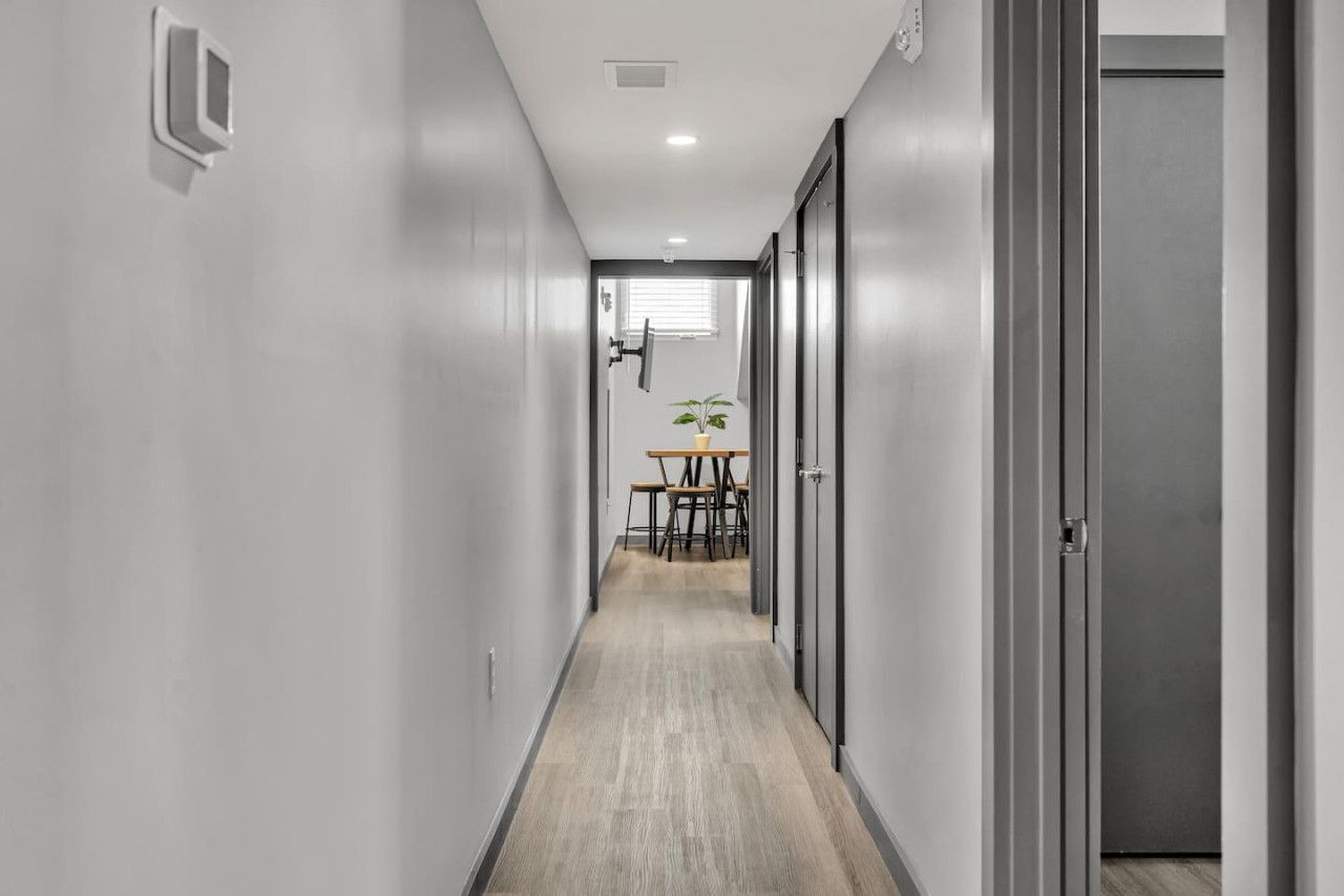 A narrow hallway with a wooden floor, a table with chairs, and a potted plant in the background.