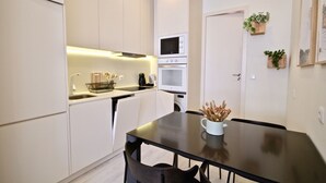 A compact kitchen with white cabinets, a microwave, and a stove. There is a dining table with chairs and a small plant on the wall. - Marjoram Apartment, Santos, Lisbon (Lisboa)