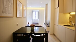 A compact kitchen with a dining area, a TV, and a window leading to a balcony. - Marjoram Apartment, Santos, Lisbon (Lisboa)