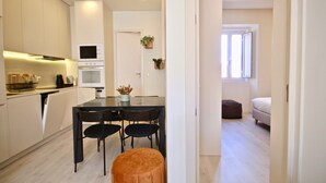 A modern kitchen with white cabinets, a dining table with chairs, and a small seating area with a bench. - Marjoram Apartment, Santos, Lisbon (Lisboa)