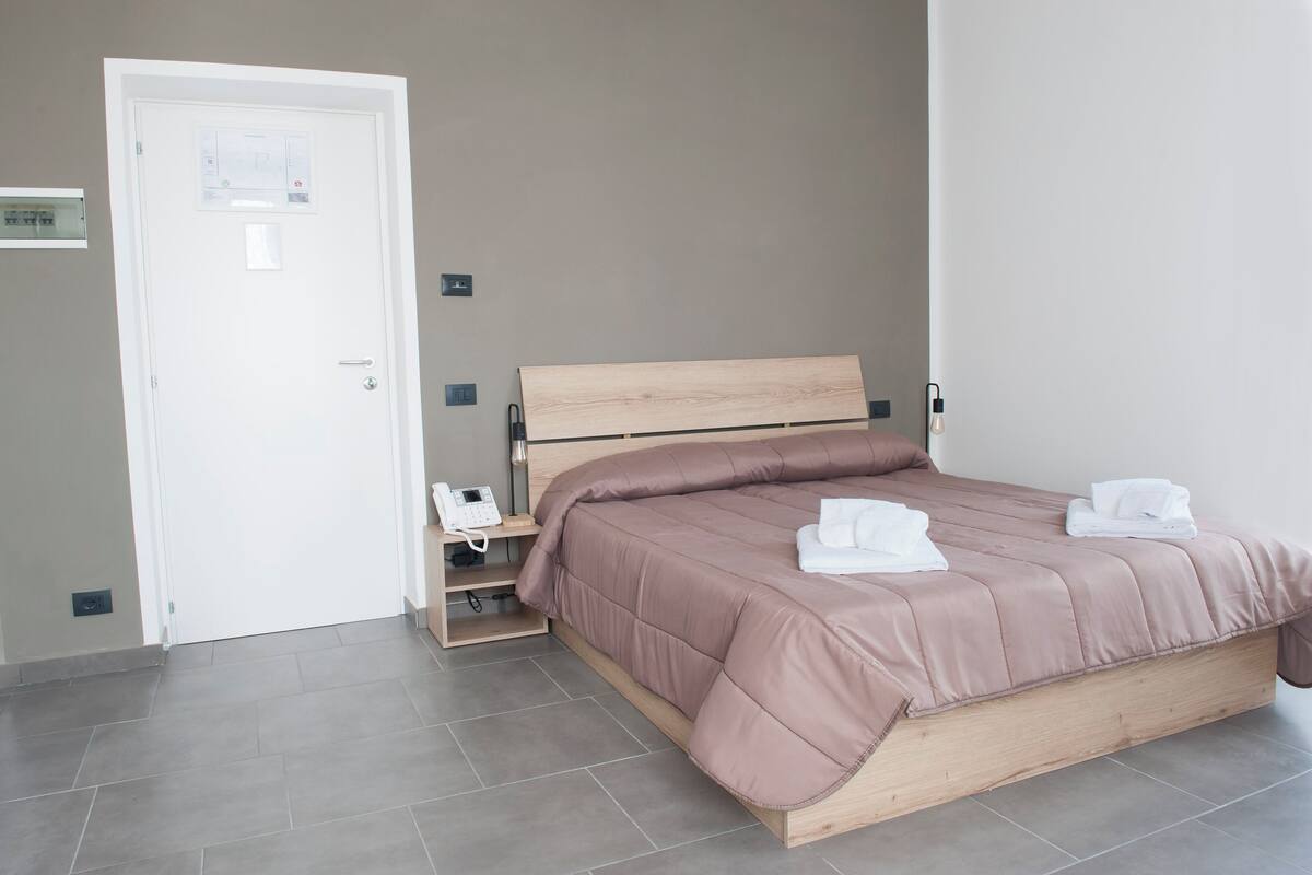 A bedroom with a wooden bed, a bedside table, a telephone, and a door with a control panel.