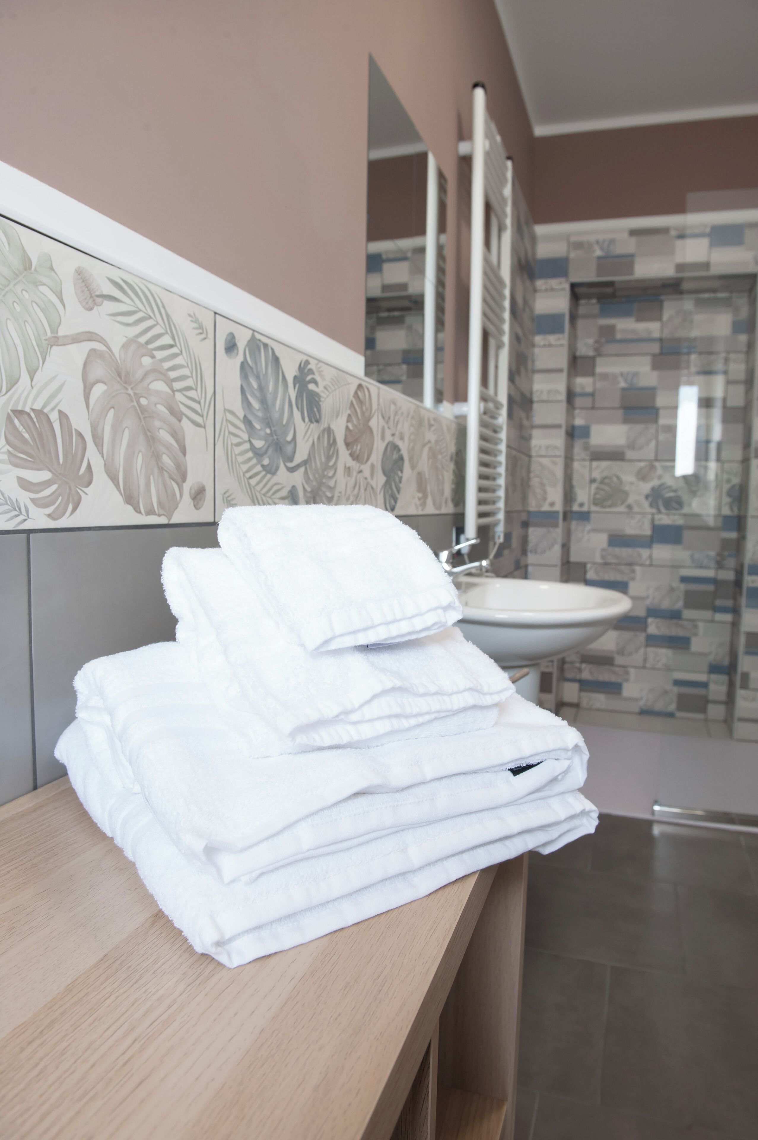 A bathroom with a stack of white towels on a wooden counter, a sink, and a mirror.