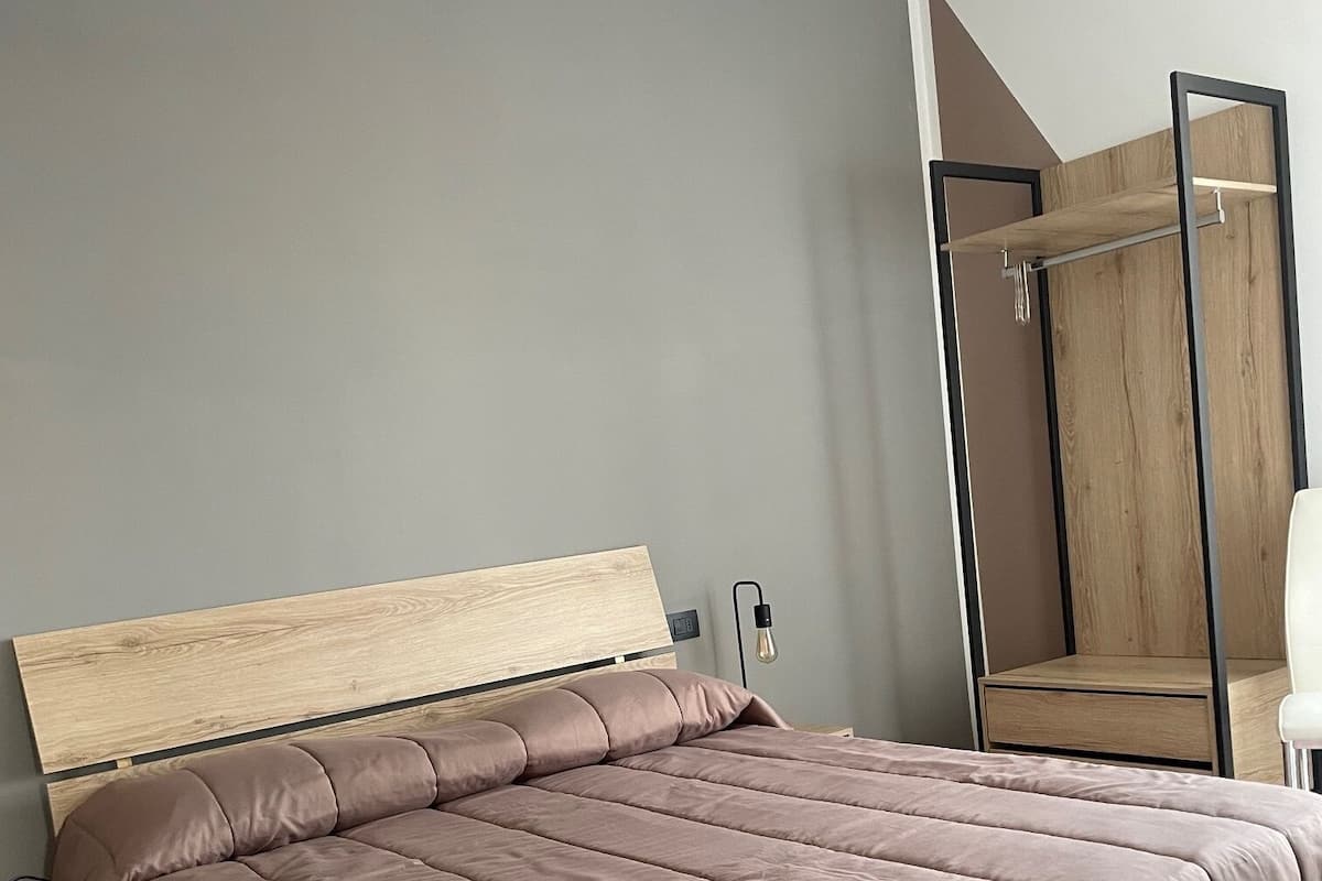 A modern bedroom with a large bed, a wooden headboard, a bedside table, and a wardrobe with a mirror.