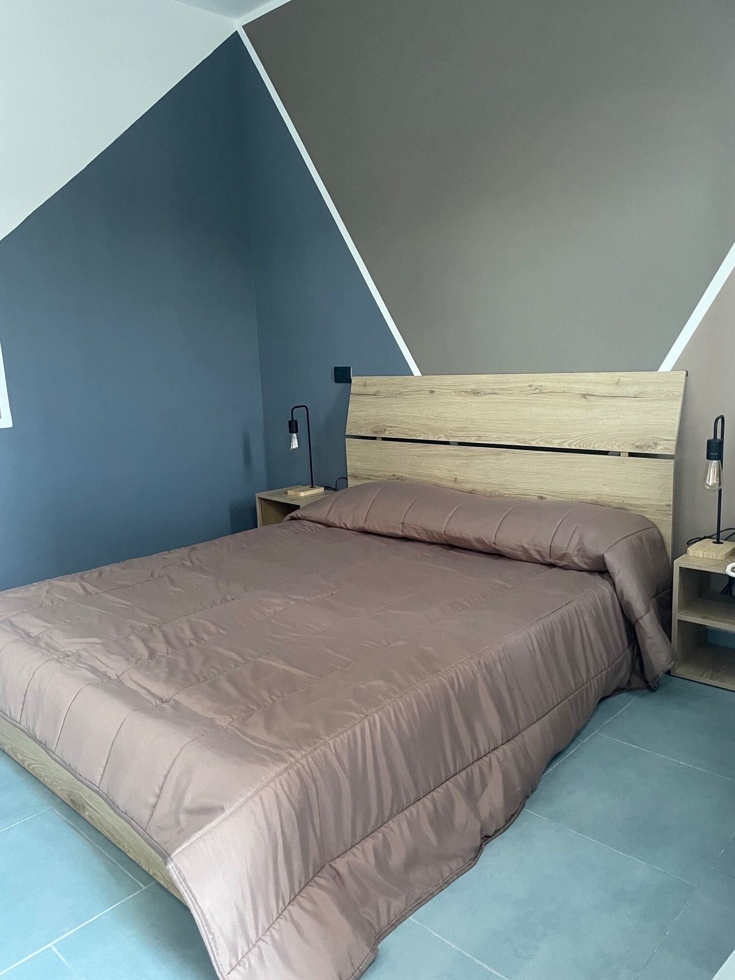 A modern bedroom with a wooden headboard, a large bed with a brown bedspread, a nightstand with a lamp, and a blue accent wall.