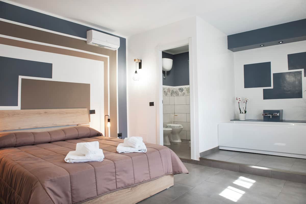 A modern hotel room with a large bed, a bathroom with a toilet and sink, and a small seating area.