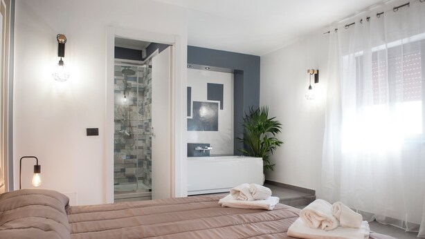 Ein modernes Hotelzimmer mit einem großen Bett, einem Badezimmer mit Glasdusche und Blick auf die Stadt.