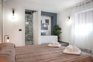 Een moderne hotelkamer met een groot bed, een badkamer met een douchecabine van glas en uitzicht op de stad.