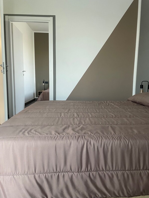 A bedroom with a large bed, a door leading to another room, and a sloped ceiling.