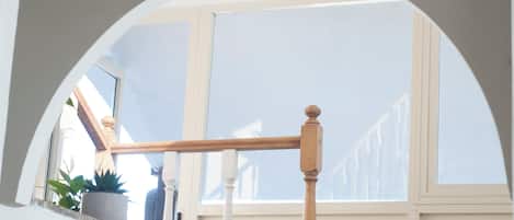 A staircase with a wooden handrail, a potted plant, and a view of a building outside.