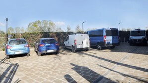 Ein Parkplatz mit mehreren Fahrzeugen, darunter ein weißer Transporter und zwei blaue Autos.
