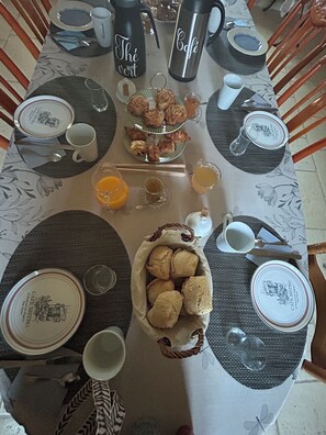 A breakfast table set with plates, cups, a thermos, and a basket of bread. - Chambre d'Hôtes Ecole de Mathuna (Jaunay-Marigny)