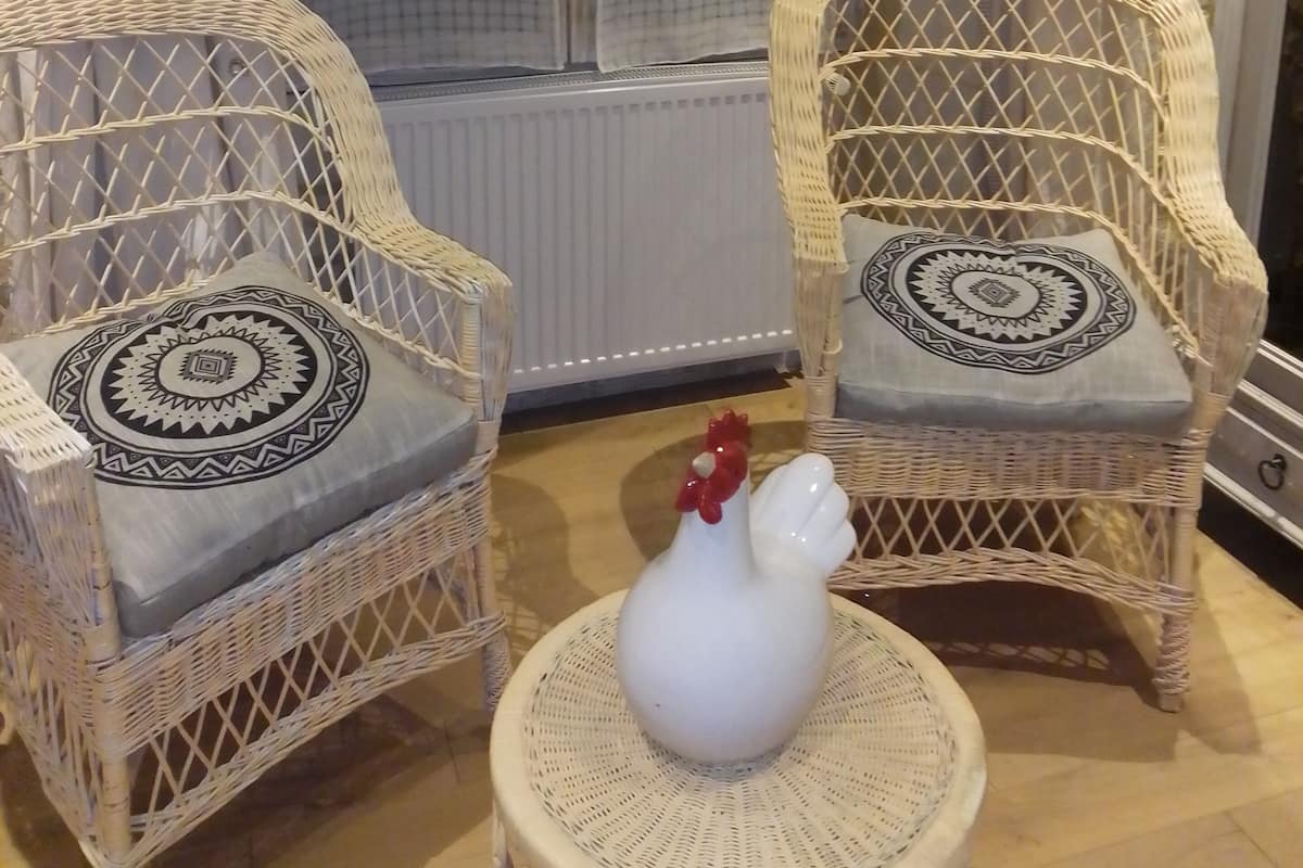 Two wicker chairs with patterned cushions, a white ceramic rooster, and a woven table.