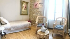 A cozy room with a bed, two wicker chairs, a small table with a vase, and a stone wall. - Chambre d'Hôtes Ecole de Mathuna (Jaunay-Marigny)