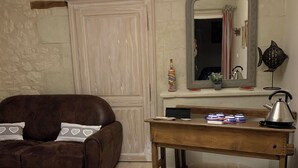 A cozy living room with a brown leather sofa, a wooden coffee table, and a white chair. A chandelier hangs from the ceiling, and a mirror with a fish-shaped frame is on the wall. - Chambre d'Hôtes Ecole de Mathuna (Jaunay-Marigny)